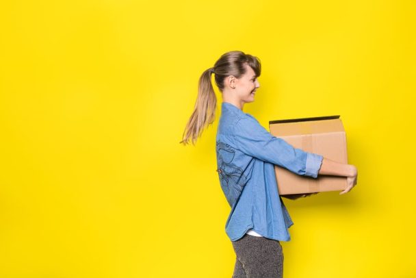 Woman carrying box on yellow background